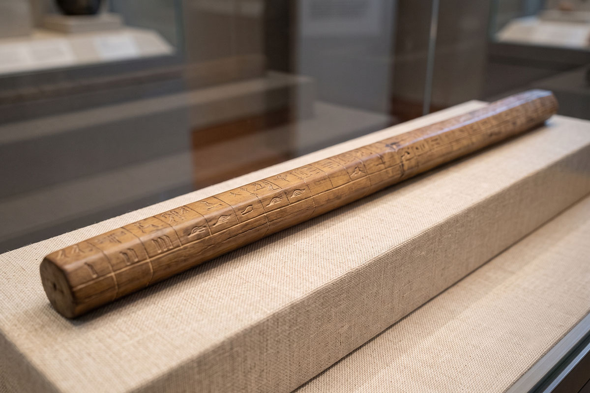 Ancient Egyptian cubit rod marked with palm and digit divisions displayed in a museum case