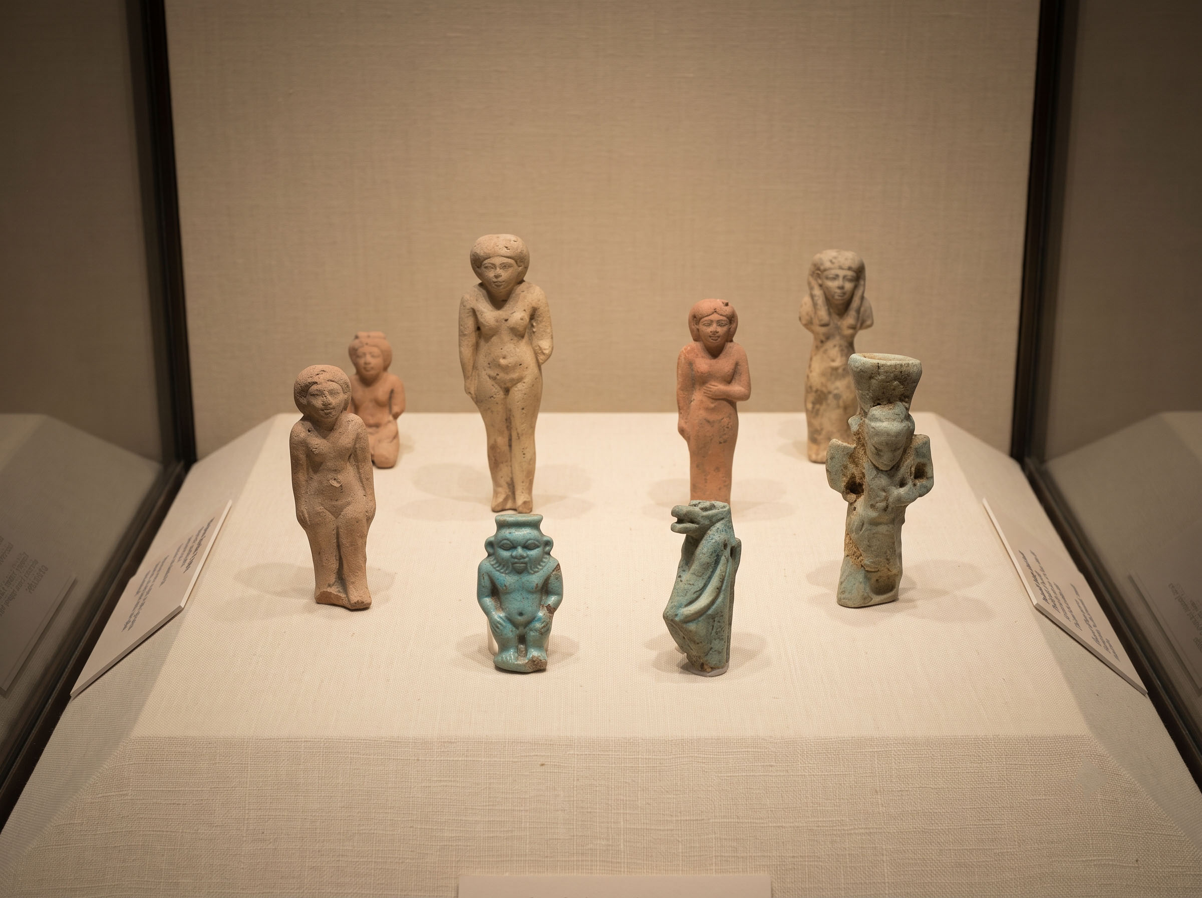 Ancient Egyptian clay votive figurines and faience protective amulets displayed together in a museum case