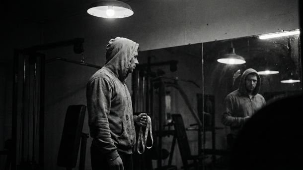 A man examining his reflection, symbolizing the pressure of male physical statistics.