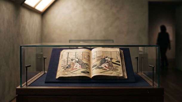 Edo-period Japanese woodblock print album displayed open in a museum vitrine under warm skylight