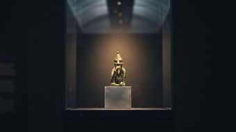 A small Viking Age bronze figurine lit in a museum vitrine, illustrating Norse mythology and the body
