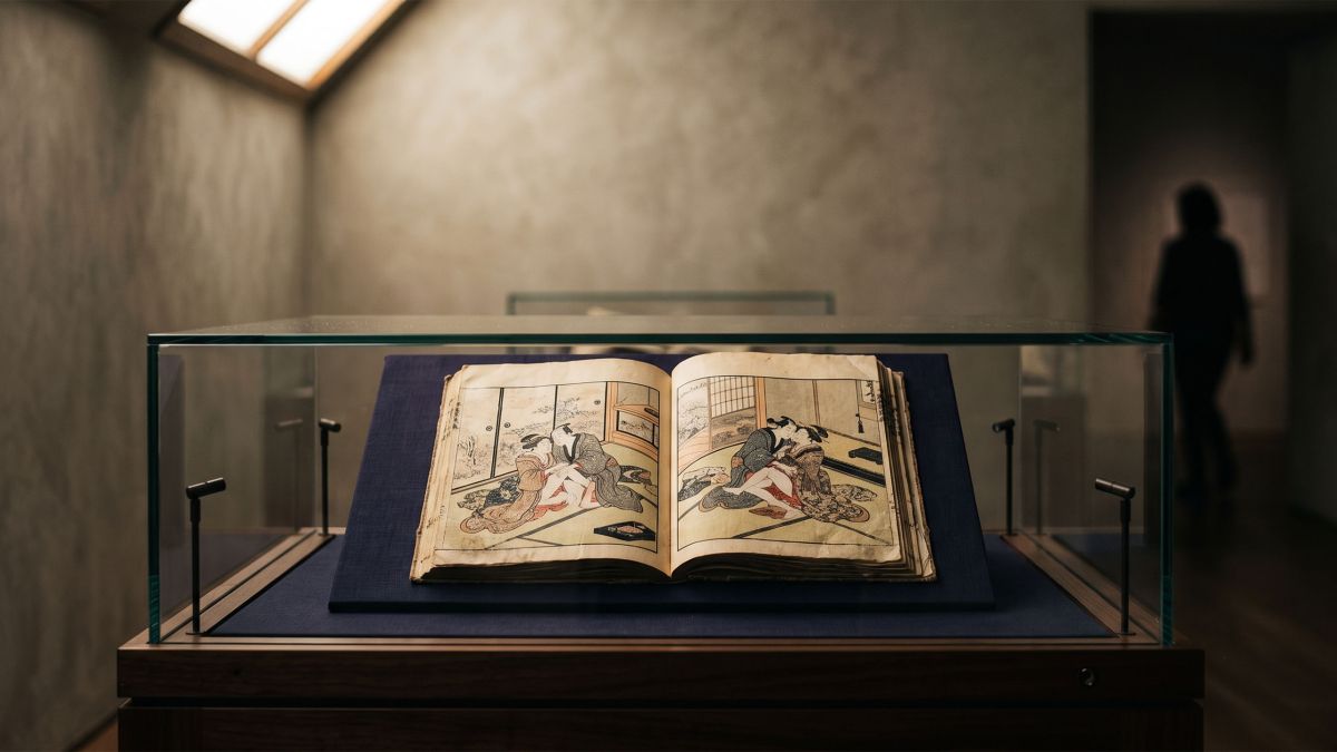 Edo-period Japanese woodblock print album displayed open in a museum vitrine under warm skylight
