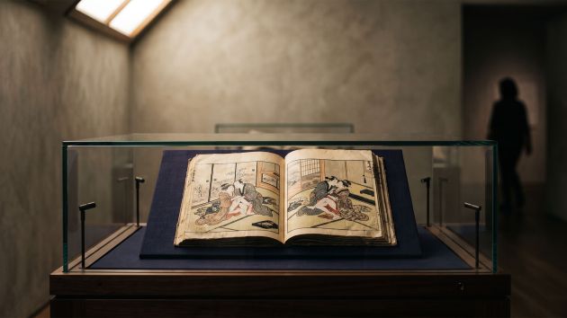 Edo-period Japanese woodblock print album displayed open in a museum vitrine under warm skylight