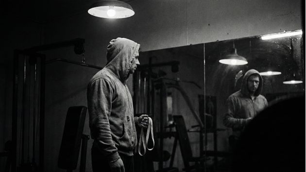 Un hombre examinando su reflejo, simbolizando la presión de las estadísticas físicas masculinas.