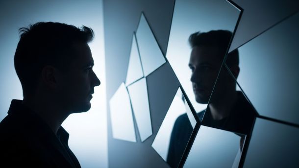Hombre frente a espejos segmentados que representan percepción vs realidad